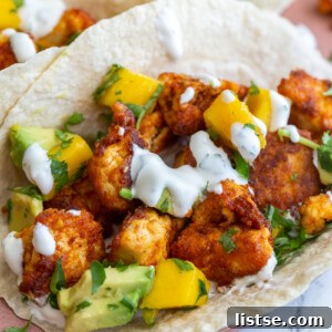 Chunks of cooked chipotle tofu in a tortilla (tacos) topped with a mango salsa and chopped cilantro. Tacos are sitting on a pink plate.