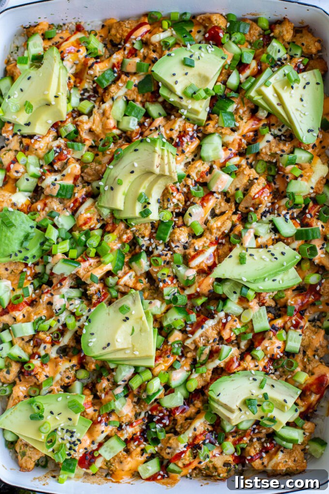 Plant-Powered Sushi Bake 5 vegetarian sushi bake inside of a casserole dish that's topped with heaps of avocado, sesame seeds and drizzled with red sriracha, orange spicy mayo, and kewpie mayo. It's also sprinkled with chopped green onion