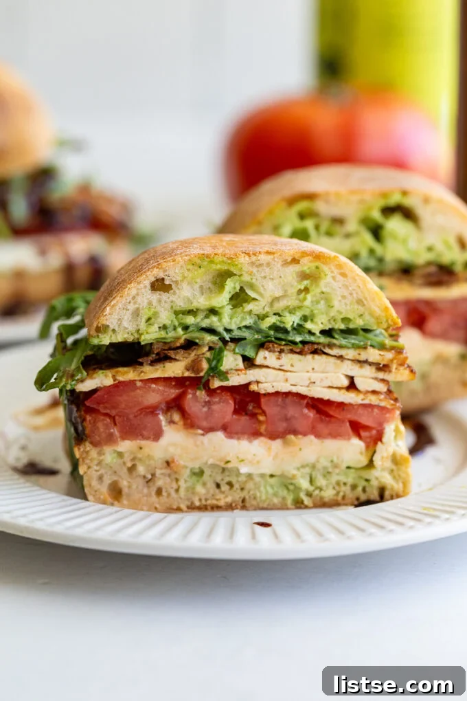 Close-up of a Tofu Caprese Sandwich, showing layers of crispy tofu, tomato, mozzarella, and basil sauce.