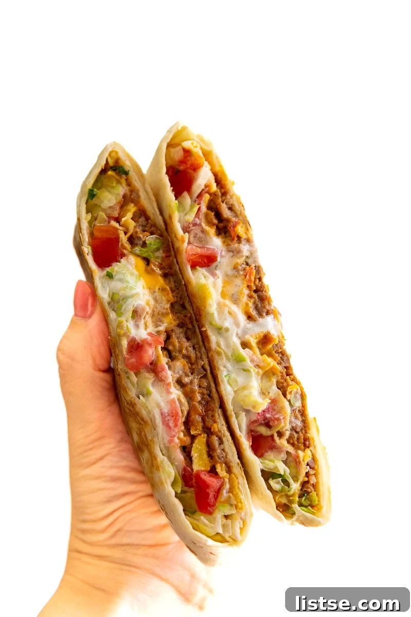 A close-up of a homemade vegan crunchwrap, showing the intricate layers of plant-based meat, melted cheese, and fresh vegetables inside a perfectly toasted tortilla.