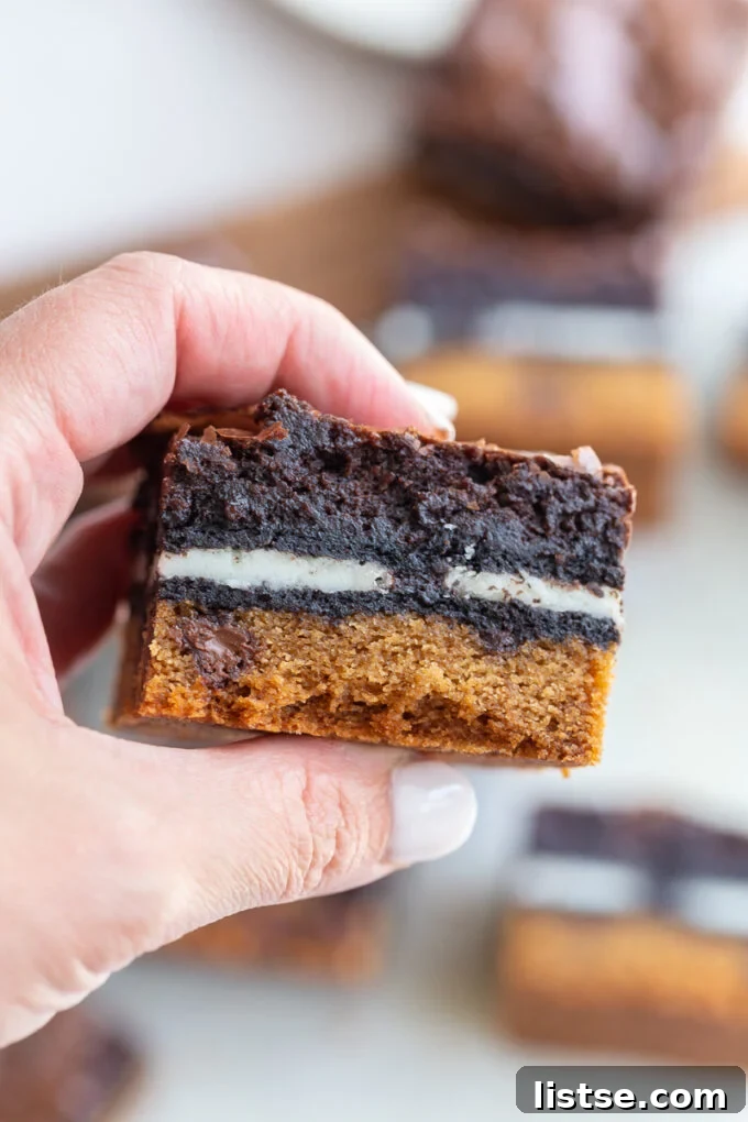 Decadent Layered Brownies 3 A close-up shot of a single layered Slutty Brownie bar, showcasing the distinct cookie, Oreo, and brownie layers.