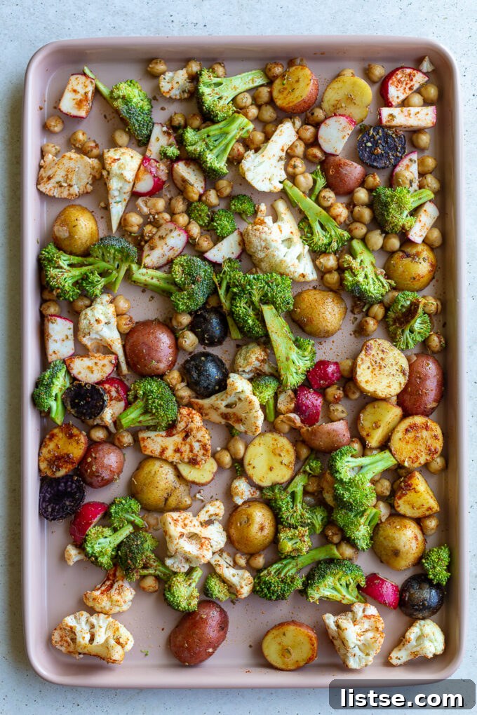A large baking tray laden with an abundance of prepped roasted vegetables: diced potatoes, quartered radishes, fresh broccoli florets, and cauliflower pieces, all ready for seasoning and roasting.