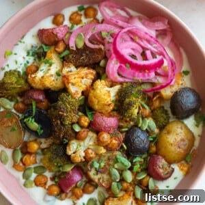 pink bowl filled with roasted veggies including chickpeas, cauliflower, broccoli, and potatoes with tzatziki underneath and pickled onion on the side