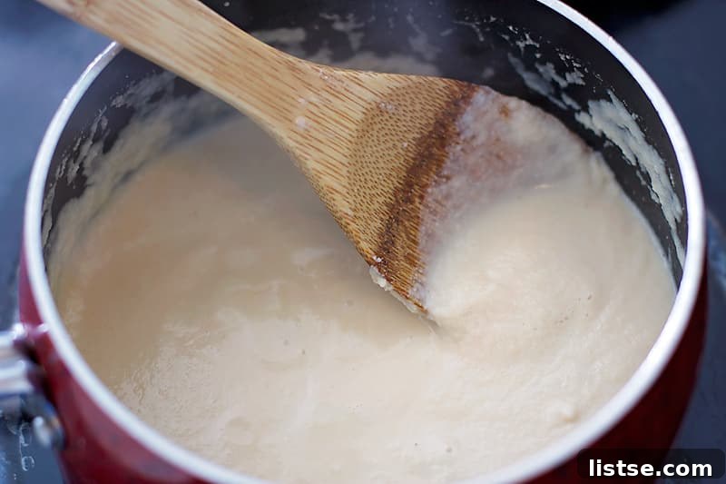 Creamy, thickened milk and flour mixture in a pan, serving as the base for the cheese sauce.