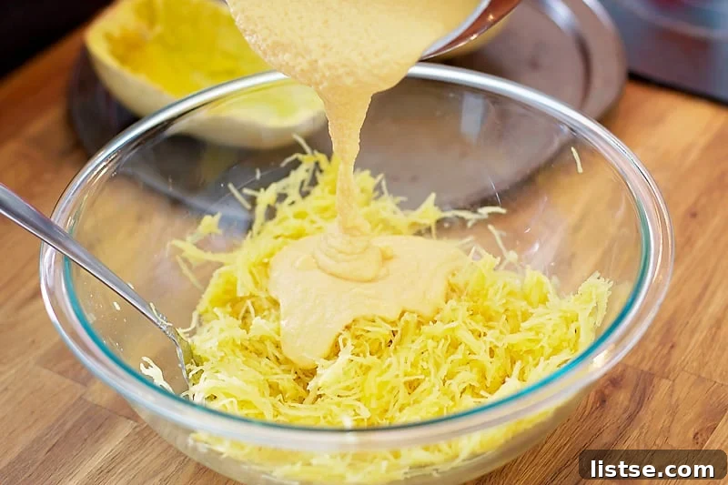 Shredded spaghetti squash being mixed with the rich, creamy cheese sauce in a large bowl.