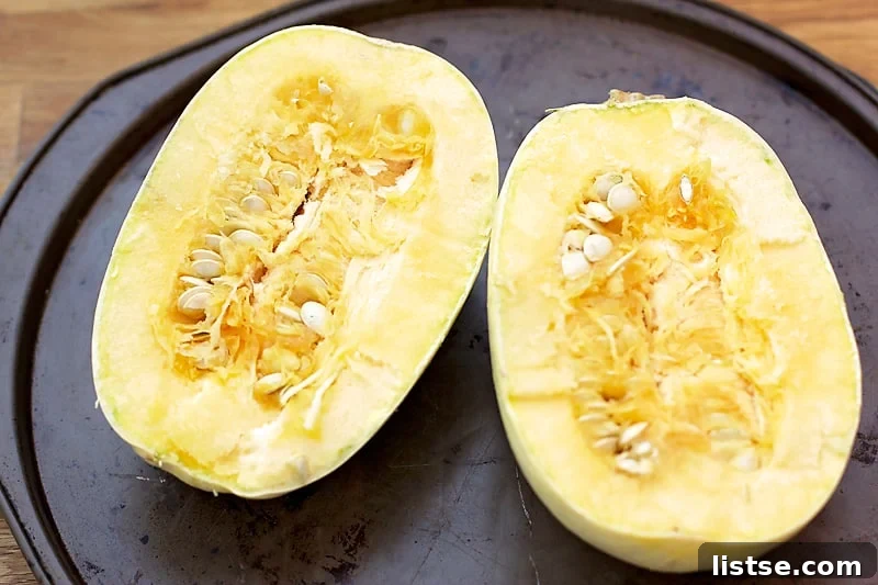 Close-up of a spaghetti squash half being scraped with a fork to remove the cooked strands.