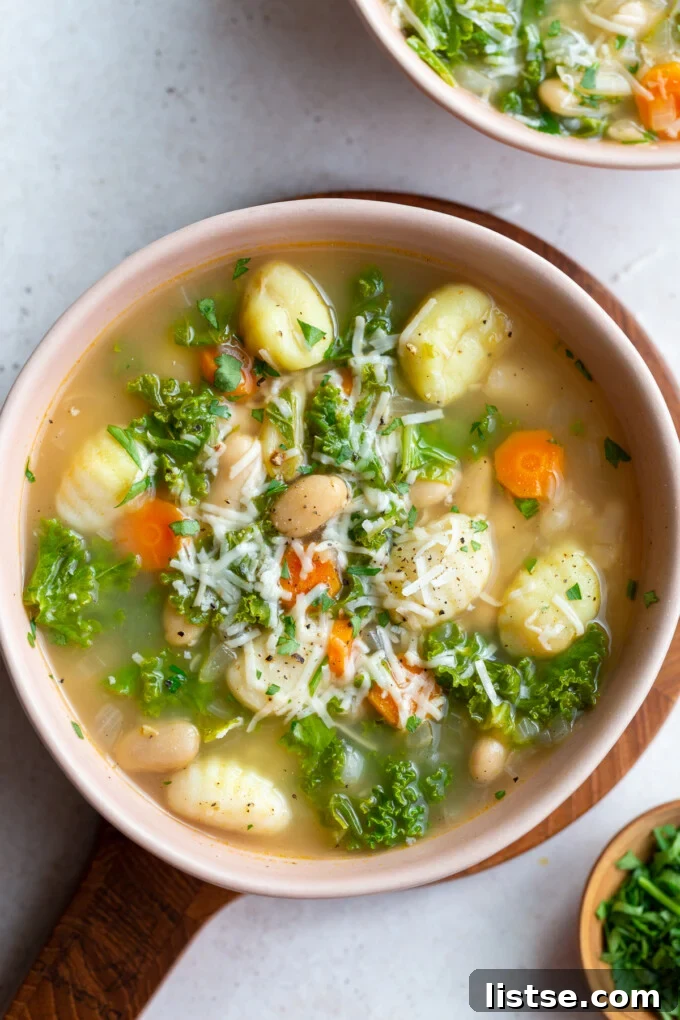 A steaming bowl of White Bean & Kale Gnocchi Soup, garnished with fresh herbs.