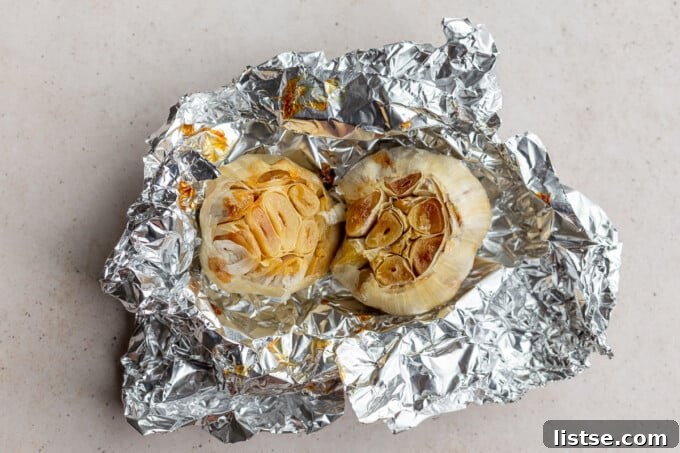 Garlic heads with tops cut off, drizzled with olive oil and wrapped in foil, ready for roasting.