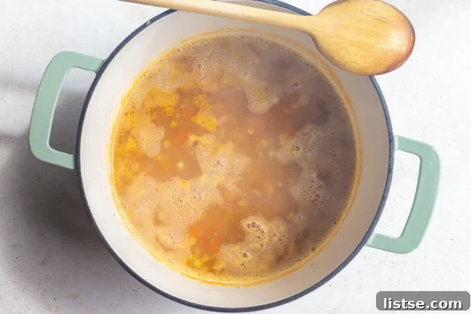 Vegetable broth, white beans, herbs, and a bay leaf added to the sautéed vegetables in a pot, simmering.