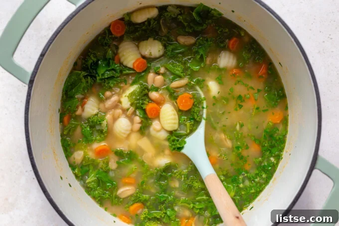A pot of creamy gnocchi soup with kale and gnocchi added, ready to be finished.