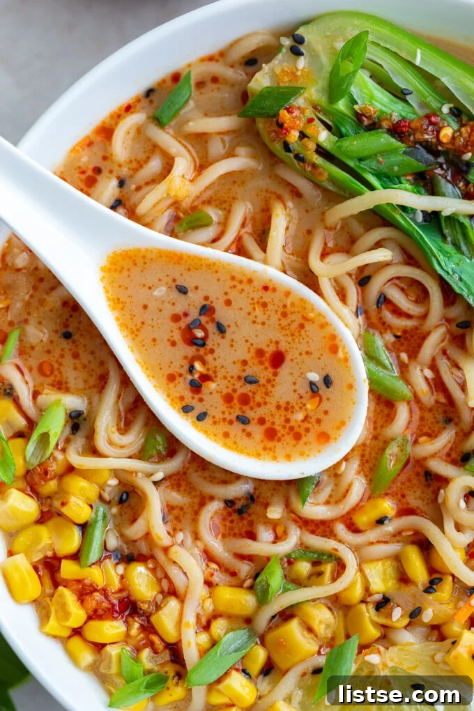 A close-up view of a spoon scooping a rich, creamy peanut miso broth with perfectly cooked ramen noodles from a steaming bowl.