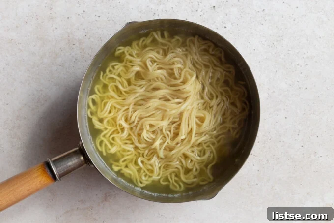 Fresh ramen noodles and blanched bok choy cooking in a pot of boiling water, preparing them for the flavorful peanut miso broth.