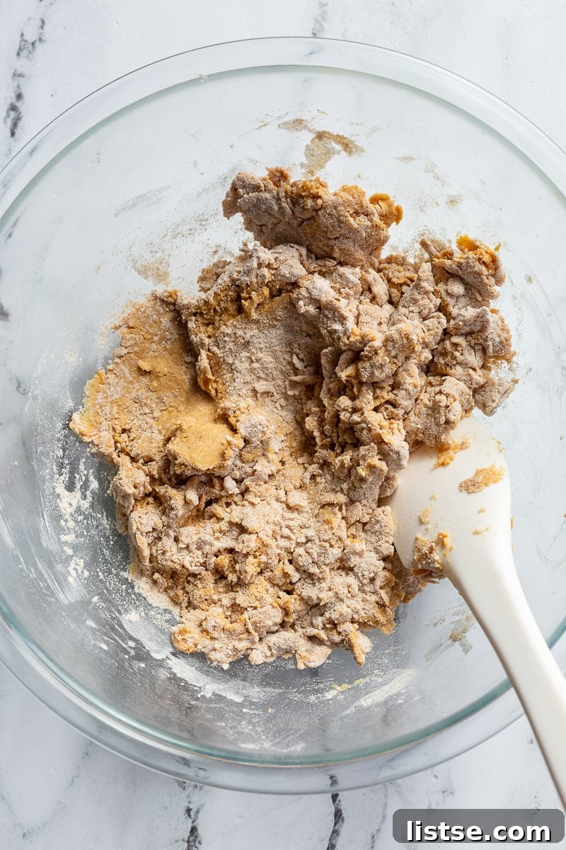 Using a spatula to stir flour with pumpkin in a large bowl.
