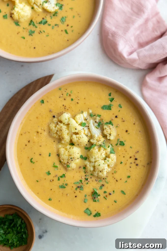Golden Roasted Cauliflower Velouté 4 A large pink bowl brimming with rich orange roasted cauliflower soup, elegantly topped with roasted cauliflower florets and fresh green herbs