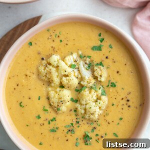big pink bowl filled with orange cauliflower soup topped with roasted cauliflower and fresh herbs