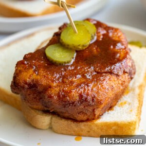 bread and fried piece of tofu covered in Nashville hot chicken sauce. It's sitting on top of slices of white bread and topped with slices of pickel