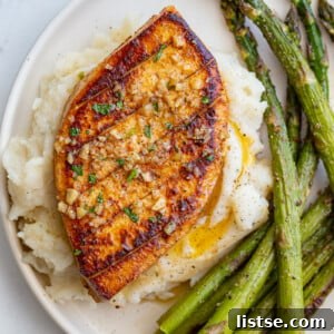 garlic butter tofu that loks a lot like a chicken breasts sitting on top of mashed potatoes with roasted asparagus on he side of the plate