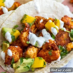 chunks of cooked chipotle tofu in a tortilla (tacos) topped with a mango salsa and chopped cilantro. tacos are sitting on a pink plate