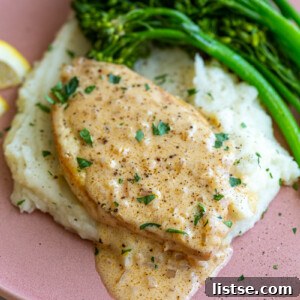 tofu slice cut in the shape of a chicken breast and topped with a chardonnay creamy sauce. The tofu is laying on top of a bed of mashed potatoes with broccolini on the side and lemon slices in the corner of the plate