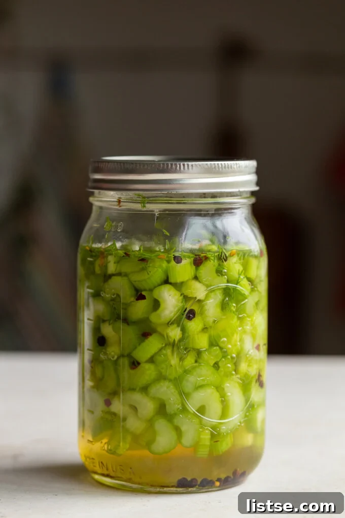 A mason jar filled with bright green pickled celery sticks, ready for refrigeration.