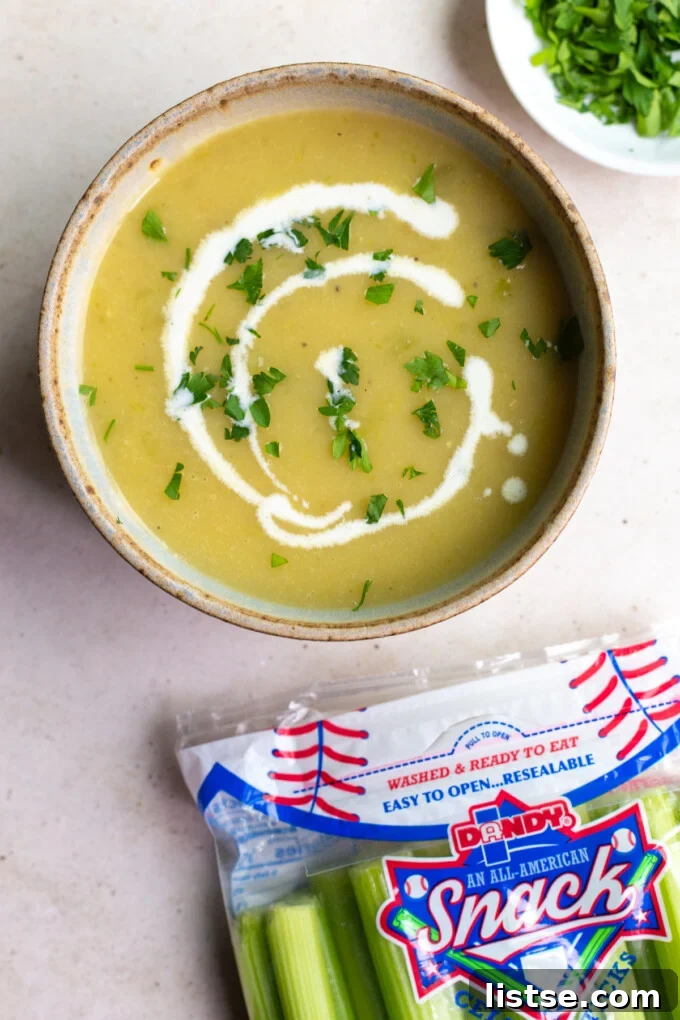 A cozy bowl of creamy celery soup, drizzled with cream, with fresh celery stalks in the background.
