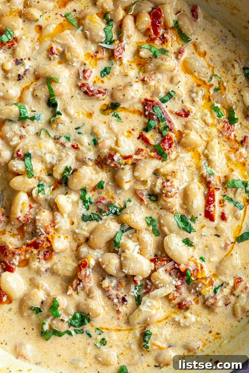 A large skillet filled with creamy butter beans and sundried tomatoes, reminiscent of 'Marry Me Butter Beans', garnished with fresh basil leaves.