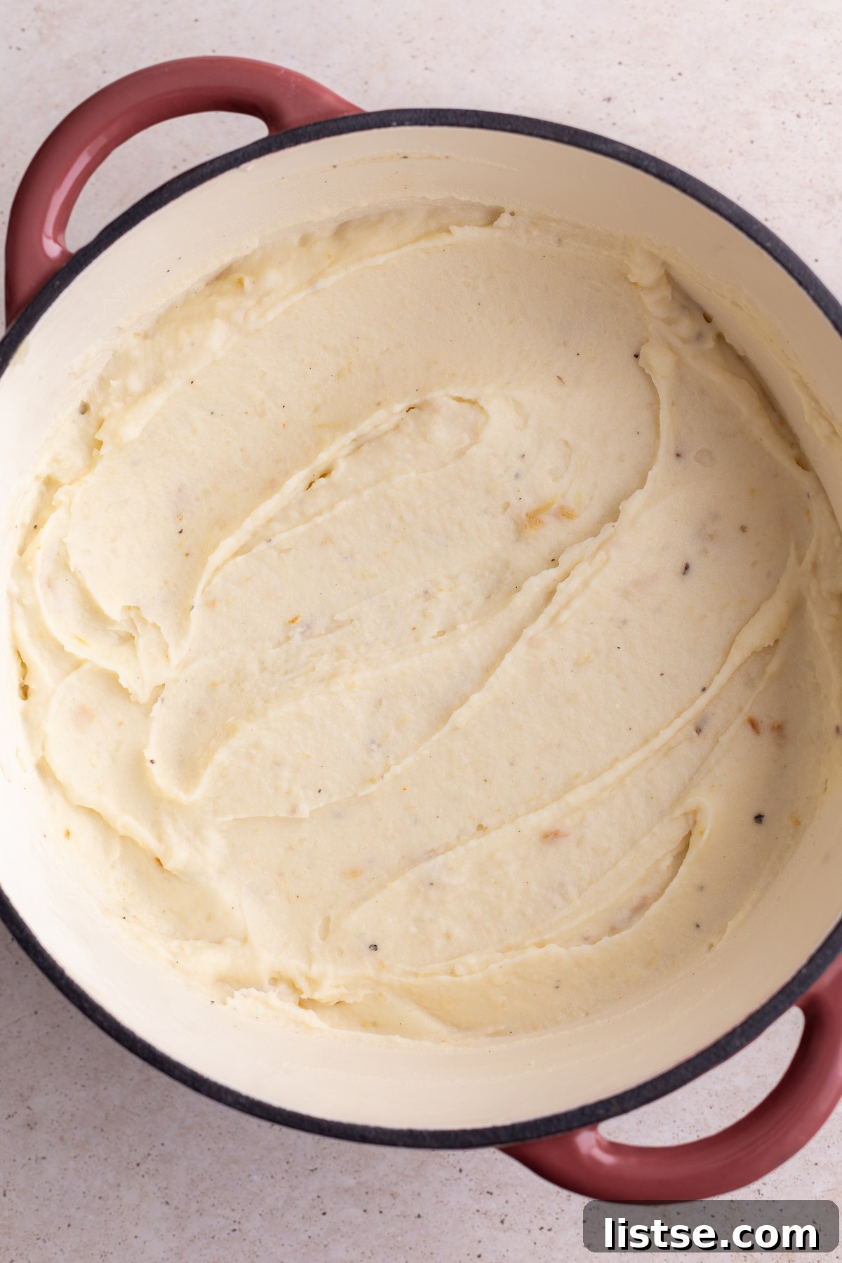Golden Roasted Garlic Mash 4 A large pink and white enamel pot filled to the brim with fluffy, freshly mashed potatoes, ready for serving.