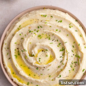 Golden Roasted Garlic Mash 7 Creamy roasted garlic mashed potatoes swirled into a pink serving dish and garnished with fresh chopped chives. A small bowl of extra chives sits in the background.