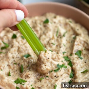 A crisp Dandy celery stick plunging into a bowl of creamy, high-protein French onion dip, highlighting its perfect texture.