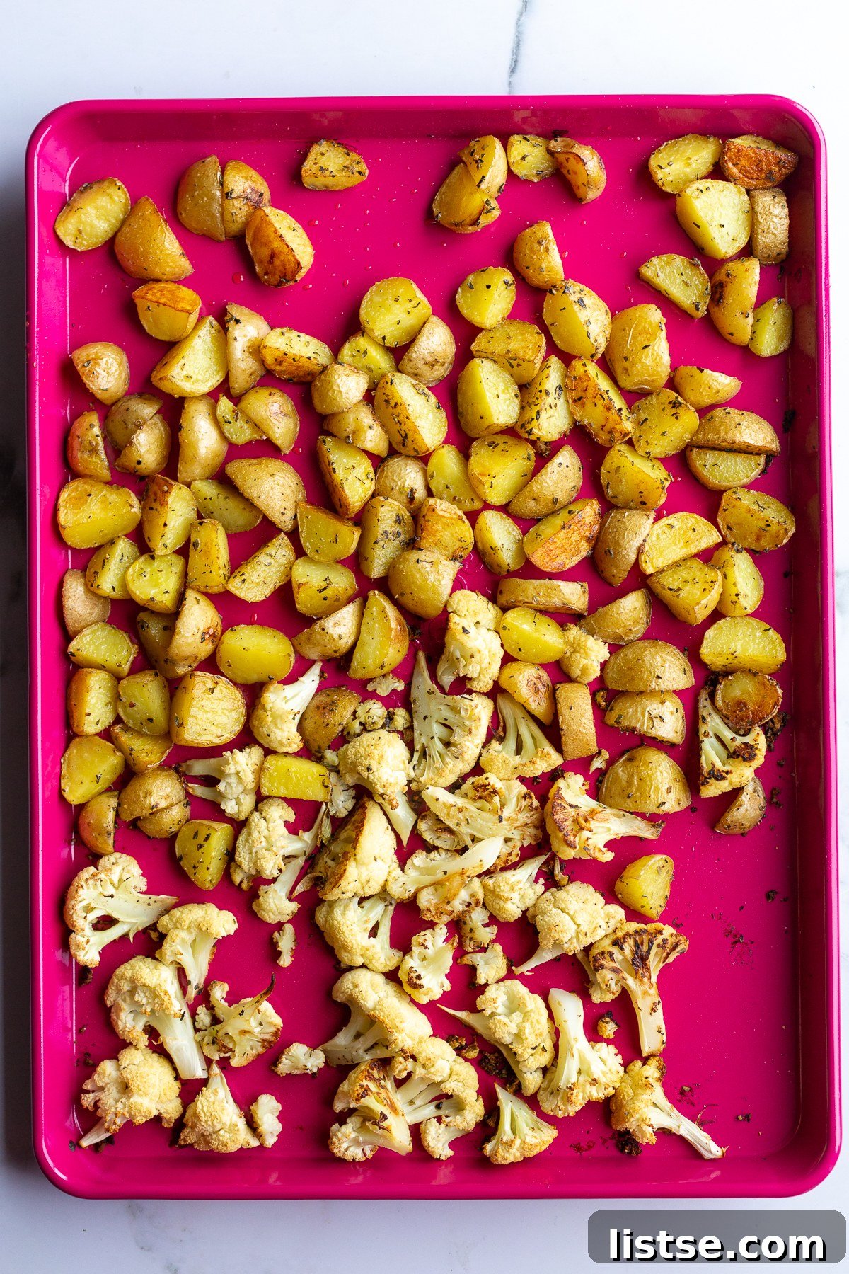 Seared Cauliflower Steaks with Vibrant Beet & Bean Puree 5 roasted baby potatoes and cauliflower on a red baking sheet