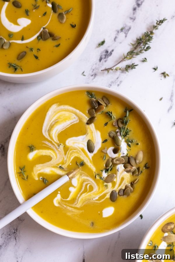 creamy vegan butternut squash soup with cream on top, garnished with pepitas, served in a white bowl on a marble board