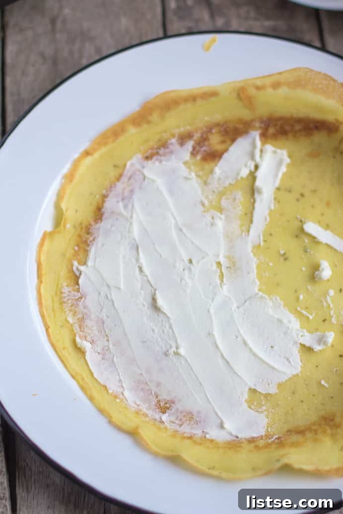 Goat cheese being spread onto a warm savory crepe