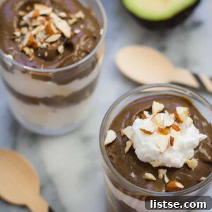 Luxurious chocolate avocado pudding in a clear glass, elegantly topped with fluffy whipped cream and a sprinkle of chopped nuts.