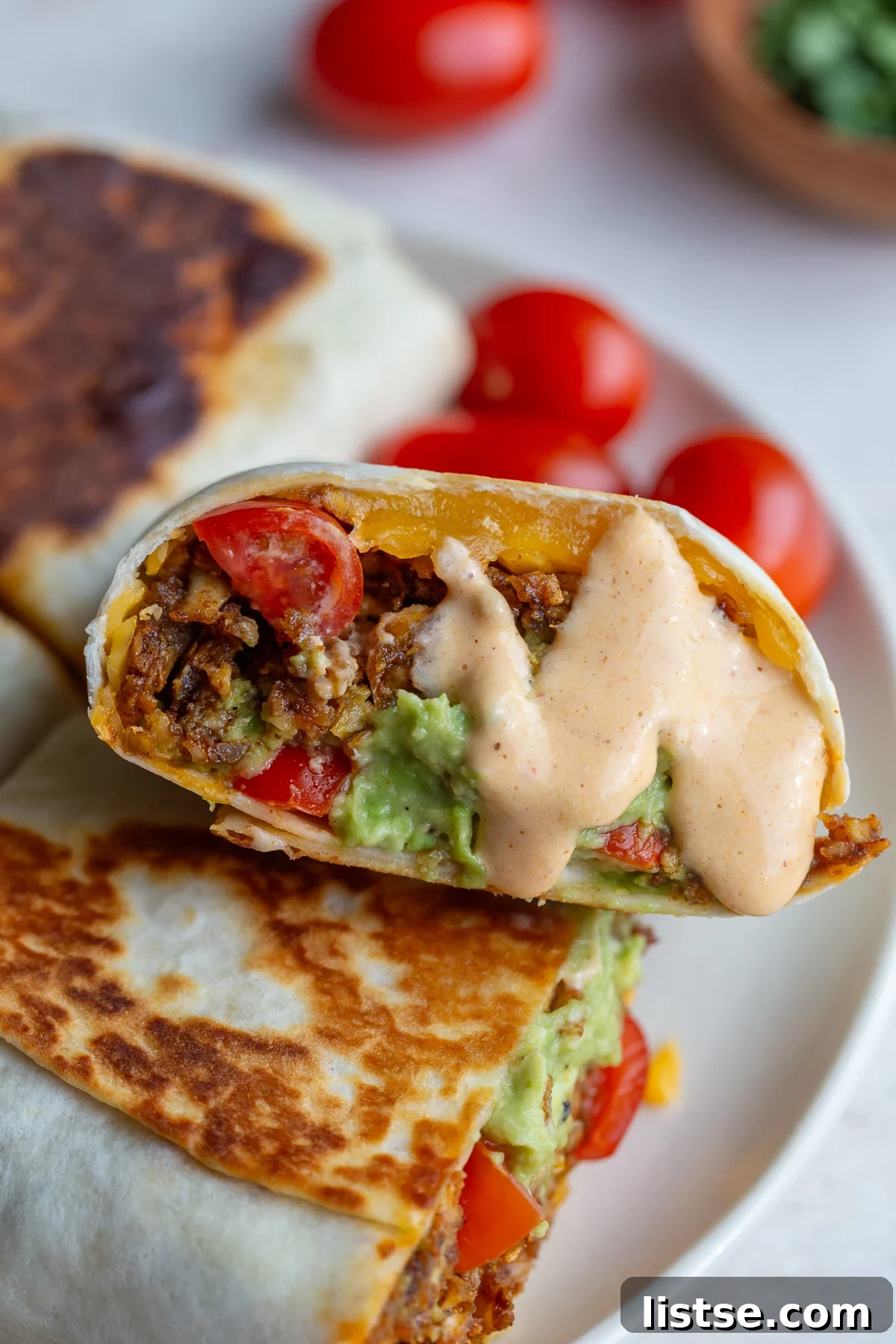 Close-up of a high protein tofu burrito drizzled with creamy cheese sauce and fresh toppings