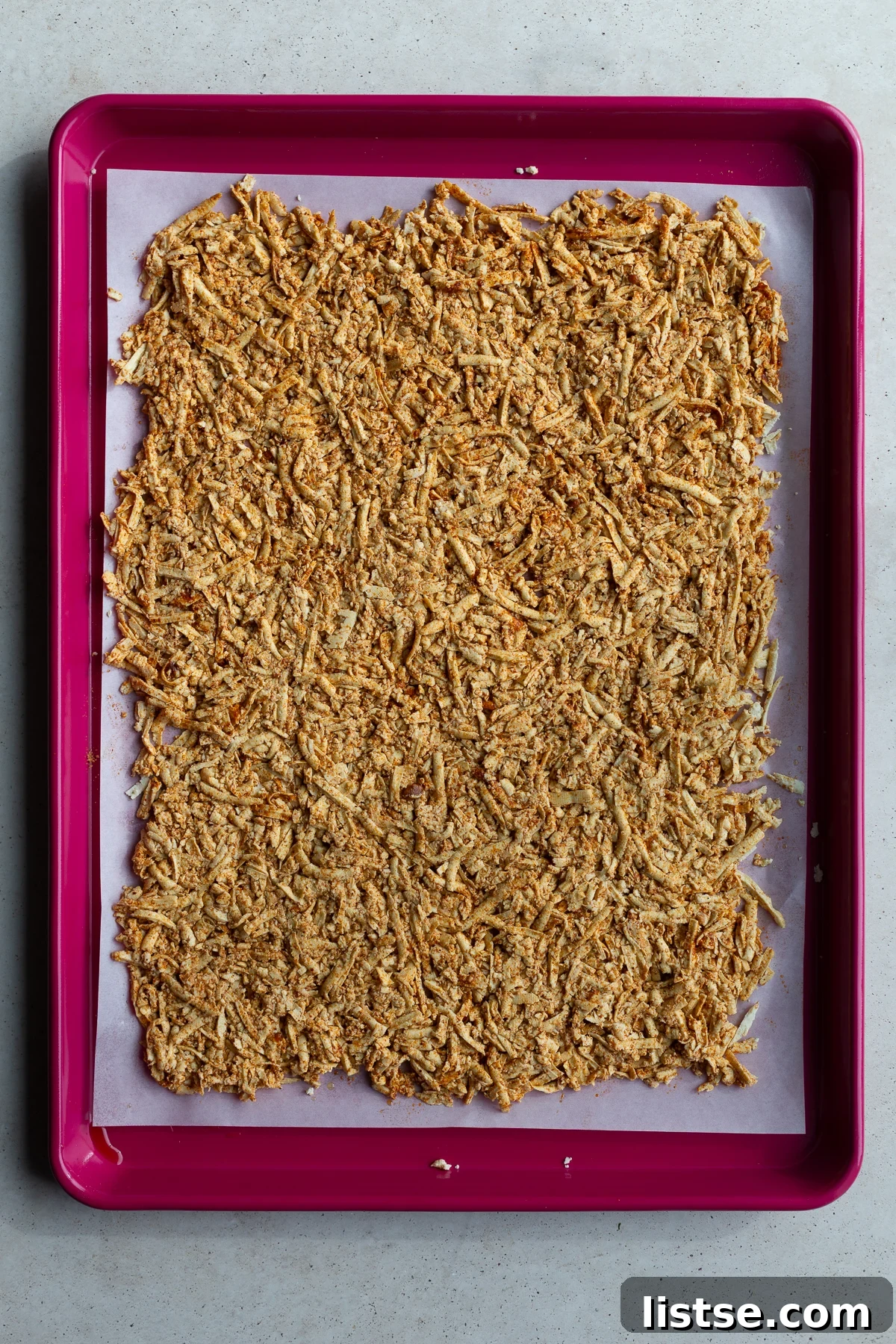 Seasoned shredded tofu mixed with olive oil and taco seasoning on a red baking sheet