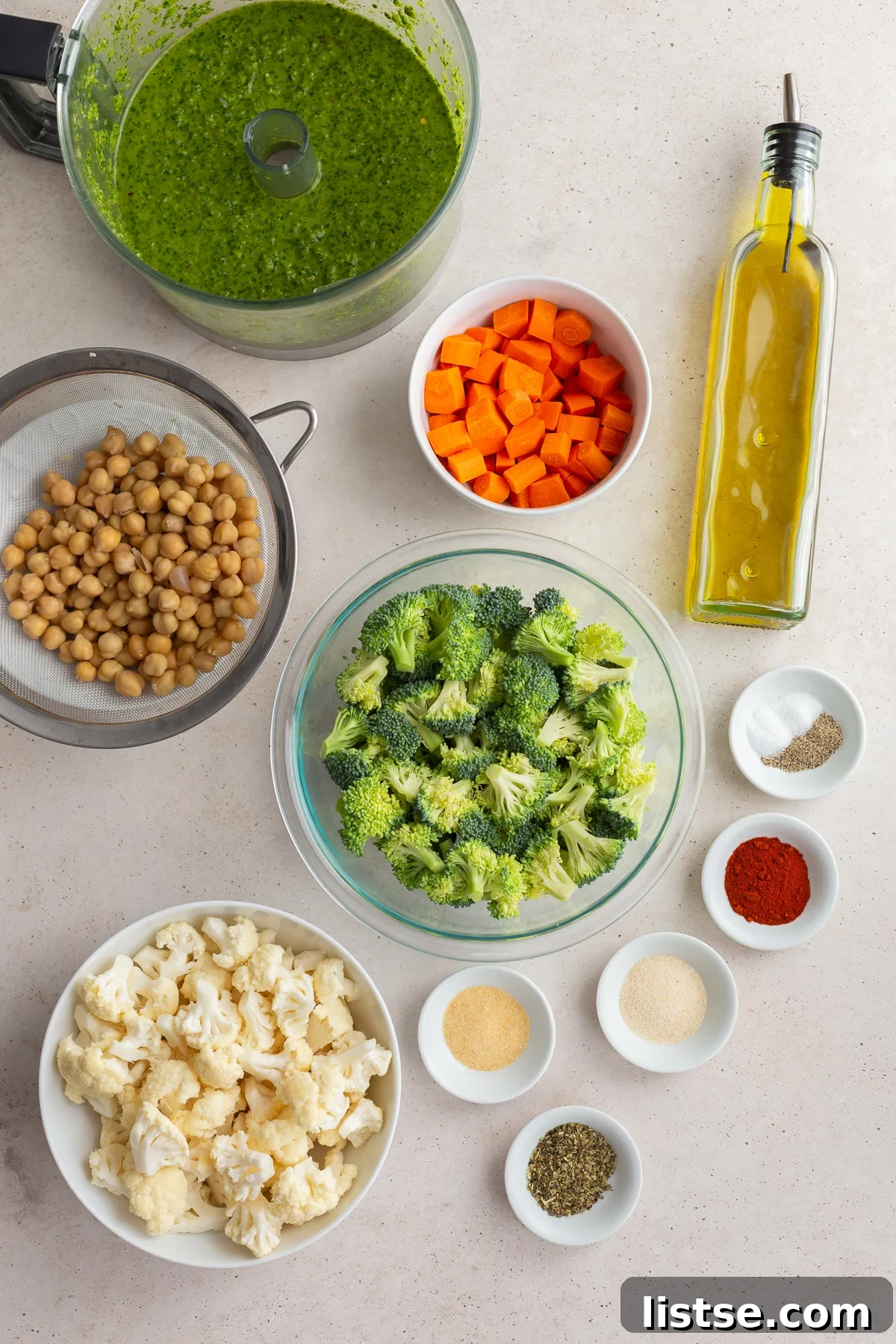 A collection of fresh ingredients laid out, including chickpeas, cauliflower, broccoli, carrots, and various spices, ready for roasting