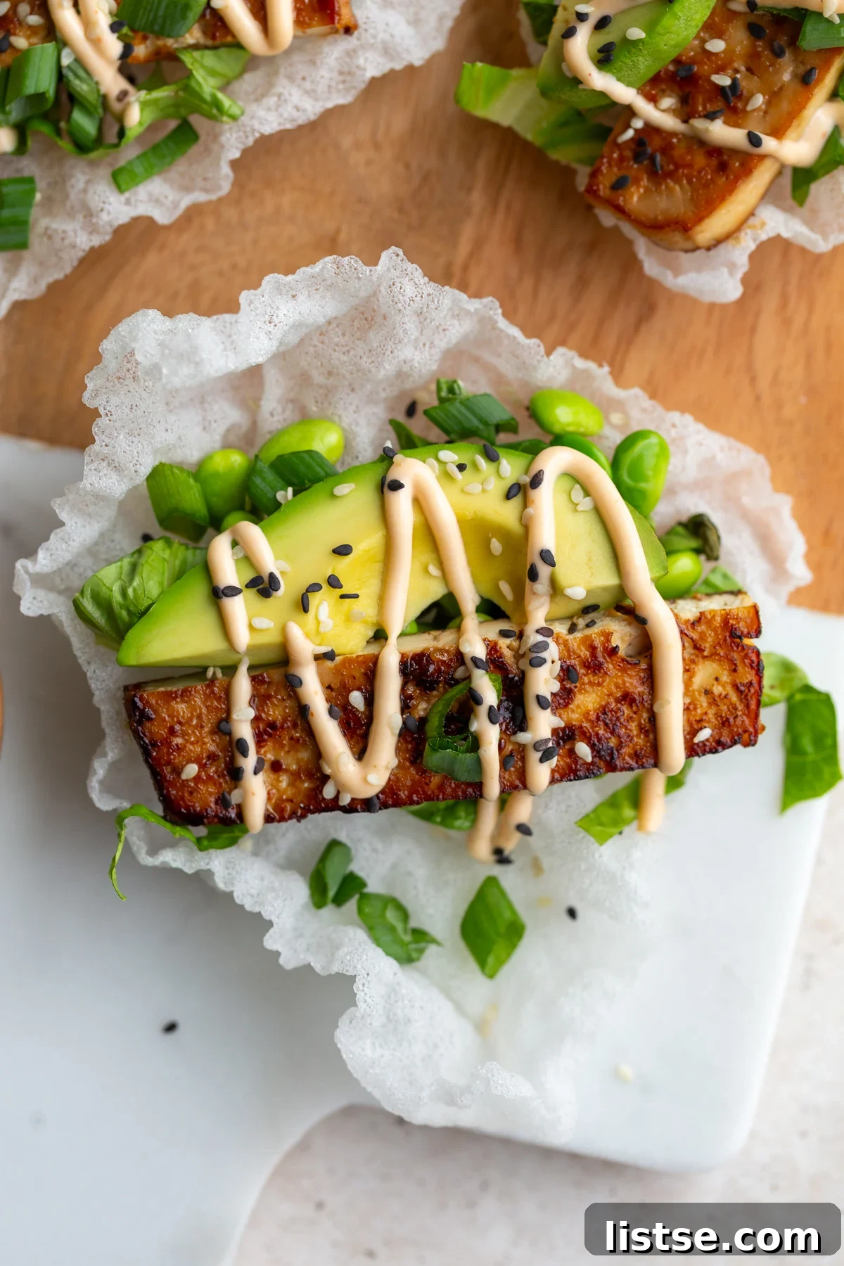 Crispy Tofu Rice Paper Tacos 3 Close-up of crispy rice paper tacos filled with vibrant ingredients like lettuce, avocado, and tofu, garnished with a spicy mayo drizzle.