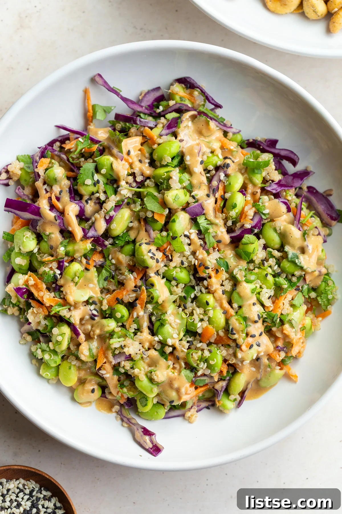 Peanut ginger dressing drizzled over an edamame salad in a white bowl.