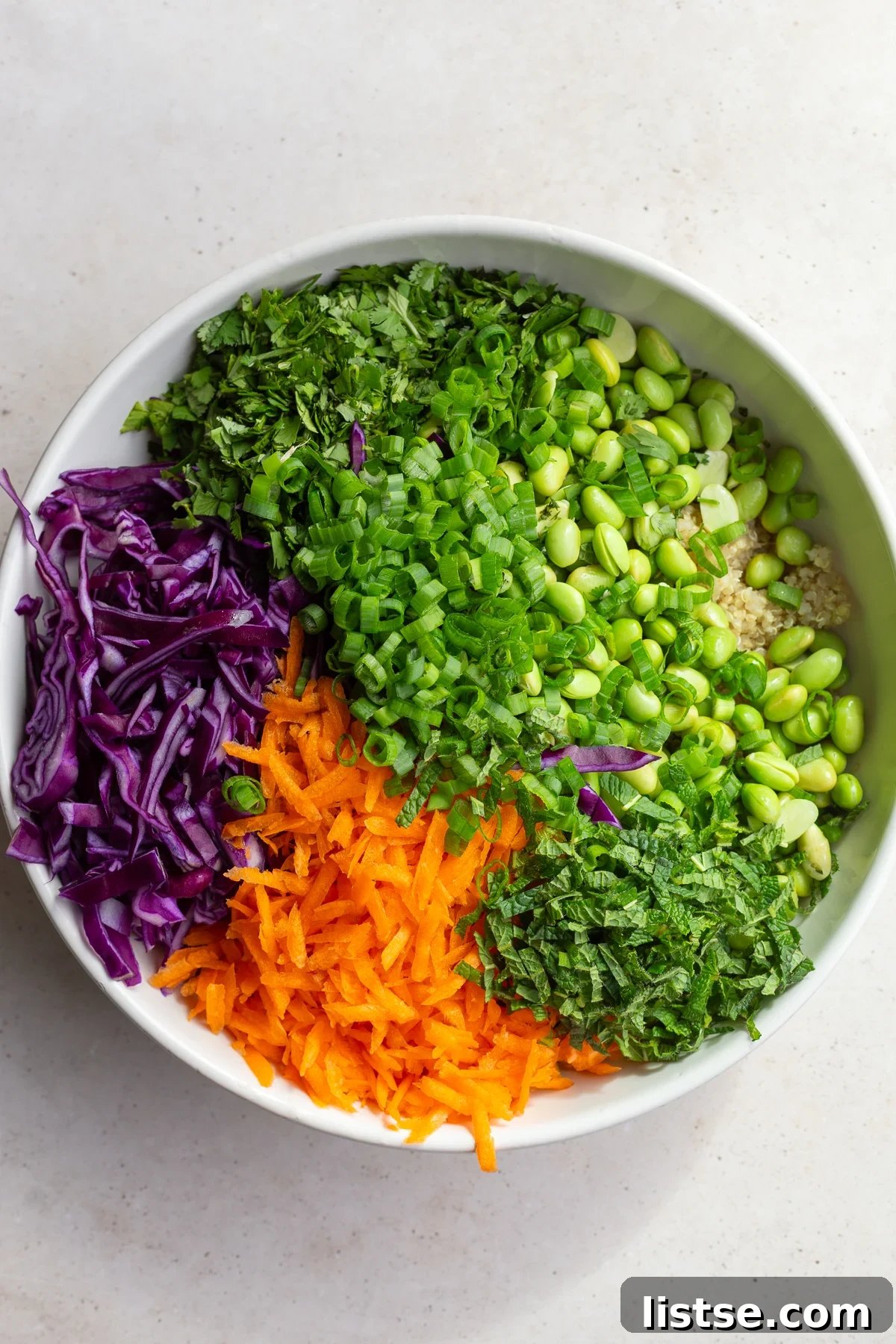 Carrots, cabbage, herbs, green onion and edamame separated into a white bowl.