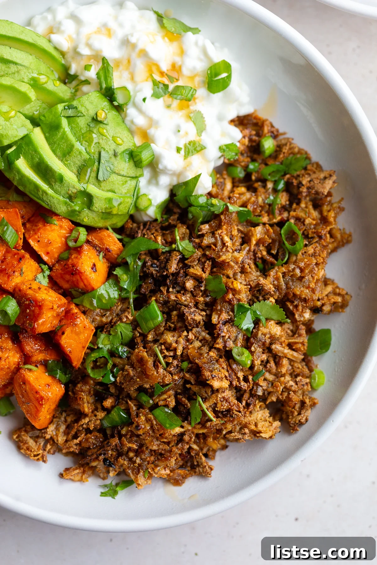 A vibrant bowl featuring seasoned tofu ground 'beef', perfectly cubed sweet potato, creamy cottage cheese, and fresh avocado slices, ready to be enjoyed.