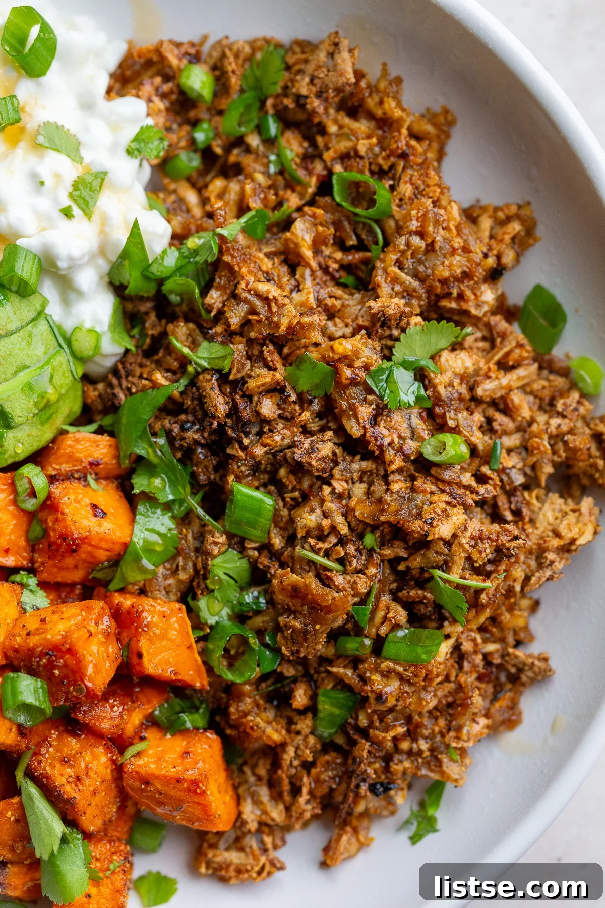 Close-up of a Tofu Ground 'Beef' Bowl showcasing the crispy seasoned tofu, roasted sweet potato, creamy cottage cheese, and fresh cilantro garnish.