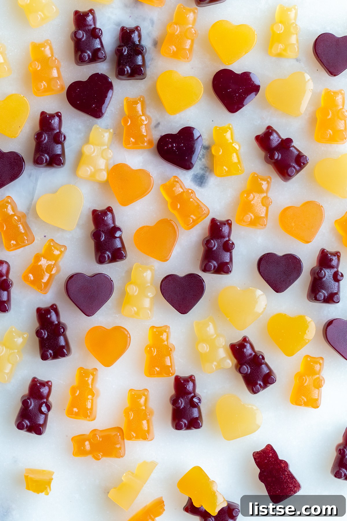 A delectable assortment of bright orange and dark red vegan gummy bears and heart-shaped gummies playfully scattered on a pristine marble countertop, ready to be enjoyed.