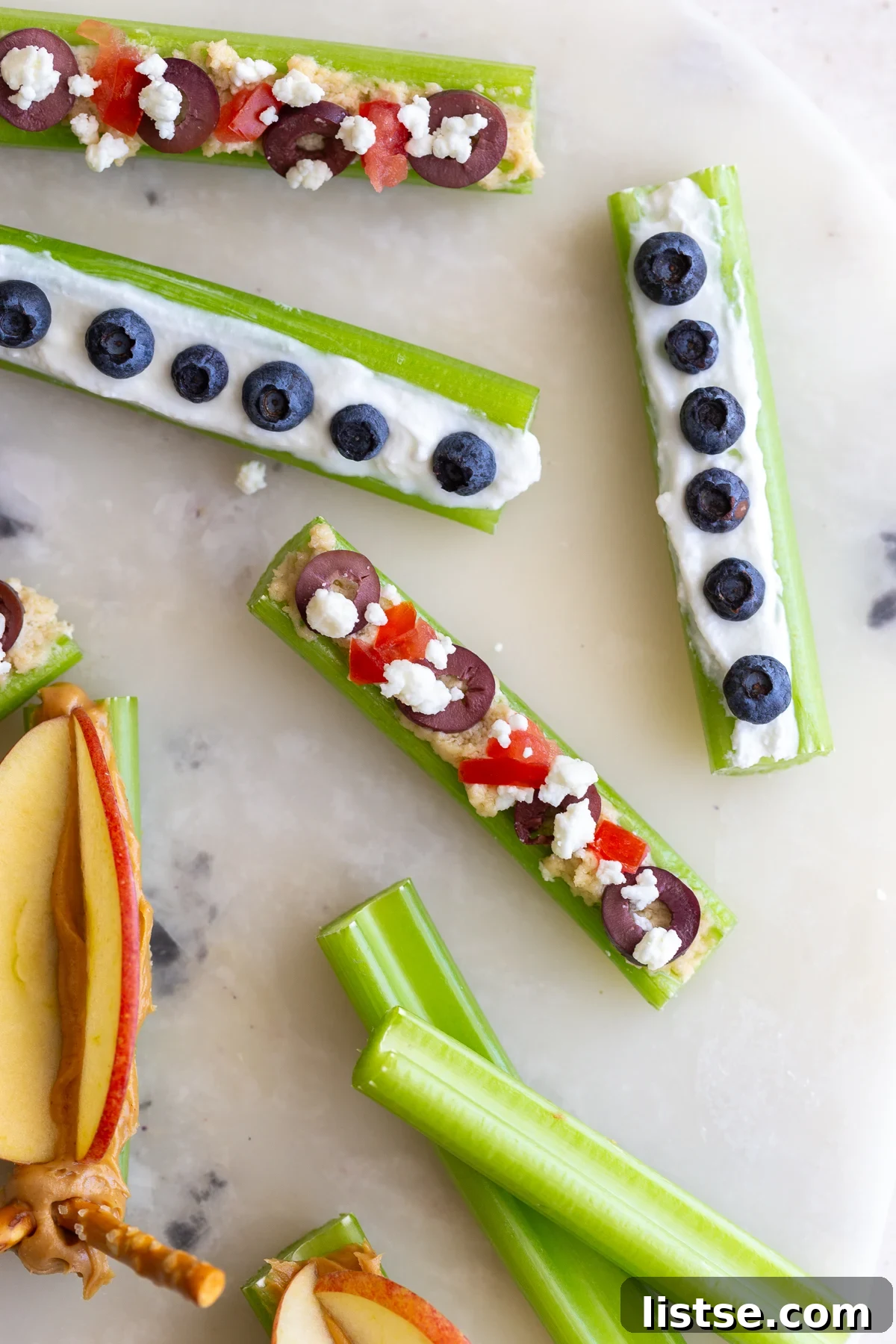 A hand holding a celery stick topped with creamy peanut butter and thinly sliced apples, designed to resemble butterfly wings.