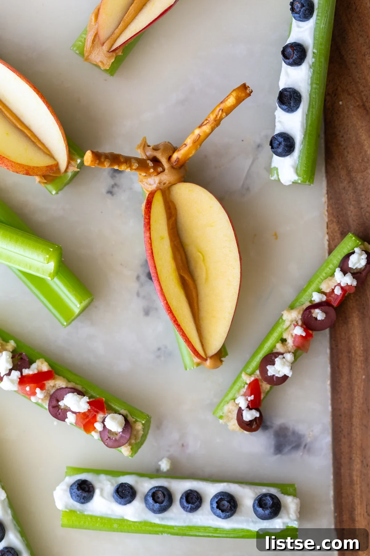 Celery sticks topped with creamy hummus, diced tomatoes, olives, and feta cheese, showcasing the Mediterranean snack variation.
