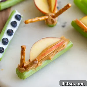 Three creative celery snack variations on a wooden board: peanut butter butterflies, yogurt and berries, and Mediterranean hummus with olives and feta.