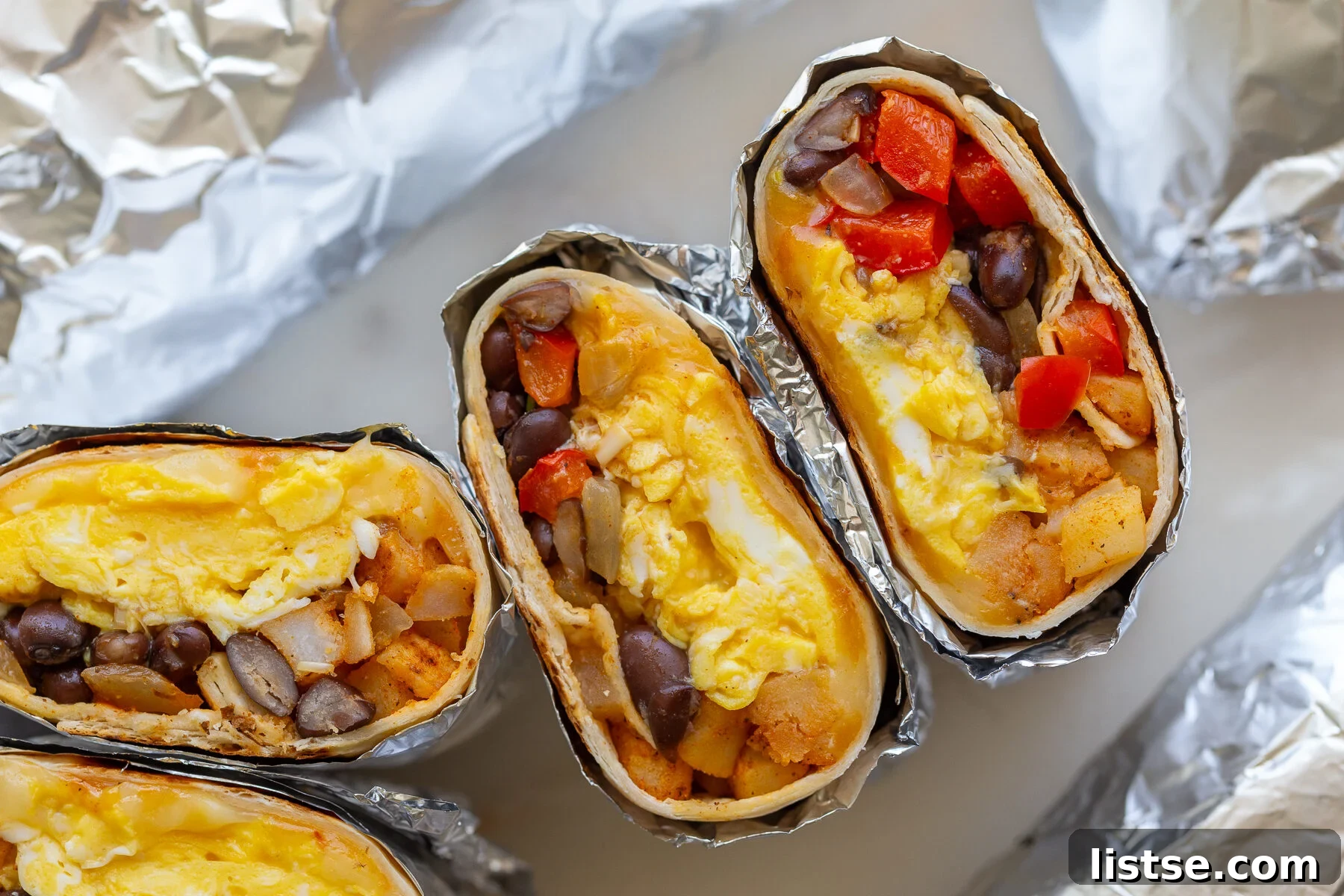Two vibrant, easy breakfast burritos, expertly cut open to display a hearty filling of fluffy scrambled eggs, colorful bell peppers, savory black beans, and crispy hash browns. This image highlights a perfect blend of ingredients for a delicious and balanced meal prep.
