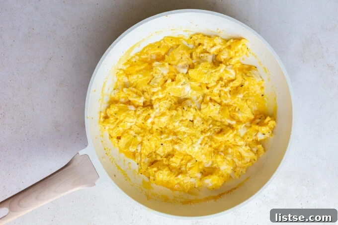 Fluffy scrambled eggs being gently cooked in the same large skillet, seasoned lightly with salt and pepper, achieving the perfect texture for a hearty breakfast burrito filling.