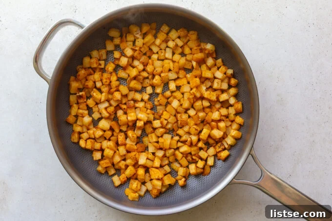 Frozen hash browns being crisped up in a large skillet, seasoned with additional spices, to create a delightful crunchy texture for the breakfast burritos.