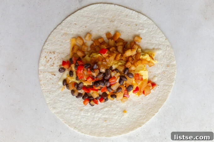 The methodical process of assembling a vegetarian breakfast burrito, layering shredded cheese, crispy potatoes, scrambled eggs, and the flavorful veggie mixture onto a flour tortilla before expertly rolling it.