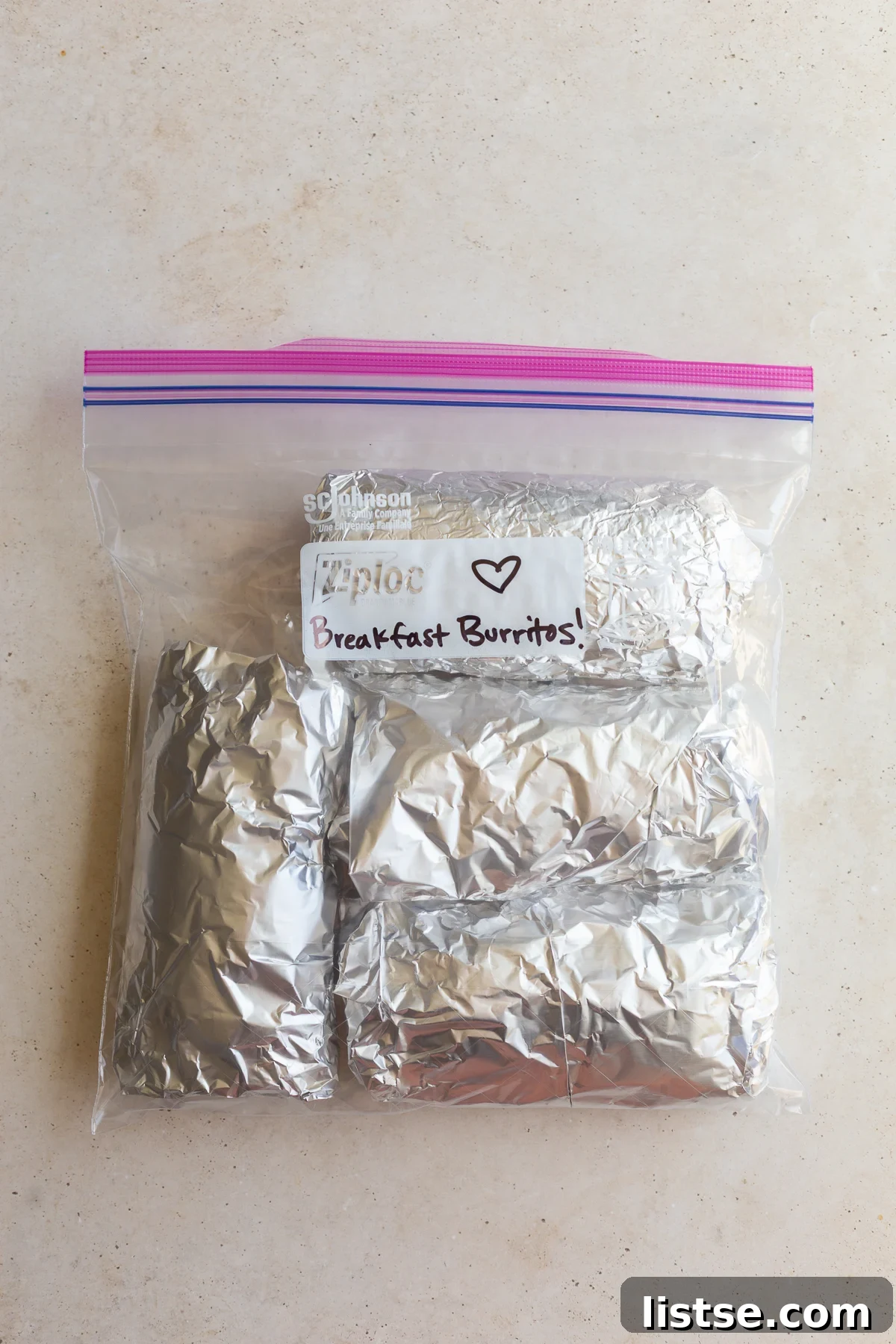 Batch of freezer breakfast burritos individually wrapped in protective foil and neatly arranged within a gallon-sized freezer bag, clearly labeled 'Breakfast Burritos!' to ensure easy identification and organized storage.